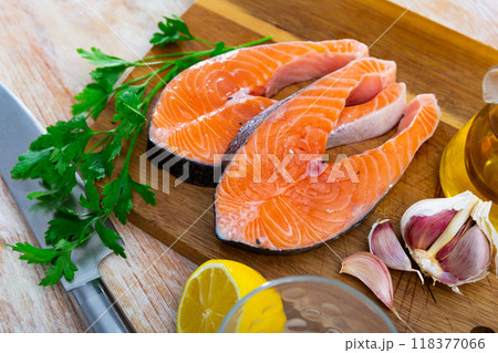 Raw salmon steaks on wooden cutting board with greens, lemon and garlic Raw salmon steaks on wooden cutting board with greens, lemon and garlic 118377066