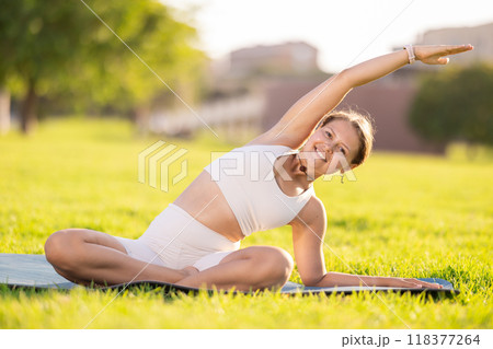 Girl in park on green grass of lawn performs lotus position, padmasana 118377264