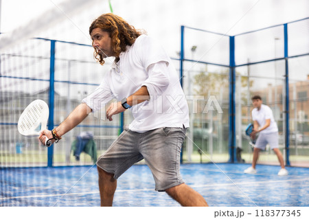 Sporty resolved man playing padel on open court Sporty resolved man playing padel on open court 118377345