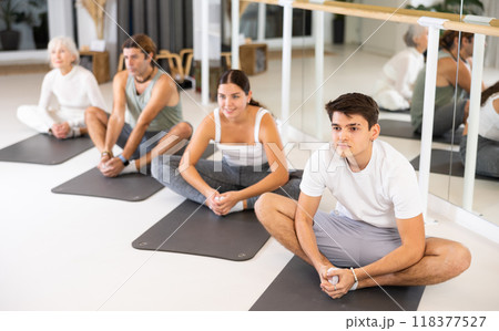 Positive athletic male performing set of exercises on a pilates mat during group class in fitness studio. Positive athletic male performing set of exercises on a pilates mat during group class in fitness studio. 118377527