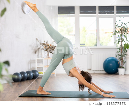 Experienced girl fitness club teacher performs downward facing dog, Adho Mukha Svanasana 118377578