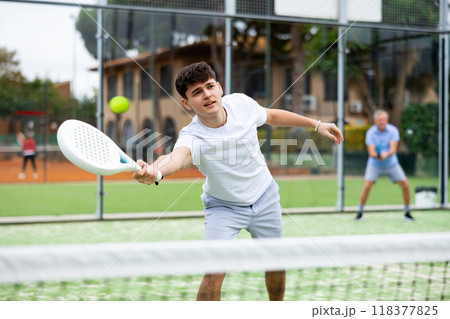 Sporty young guy playing padel on open court 118377825