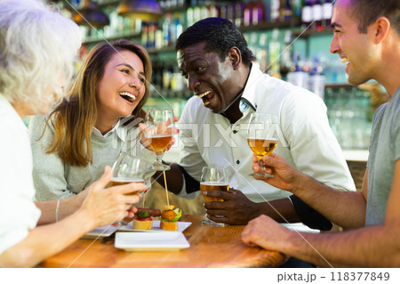 Company of multiracial friends drinking beer and talking with each other during the rest in a pub 118377849
