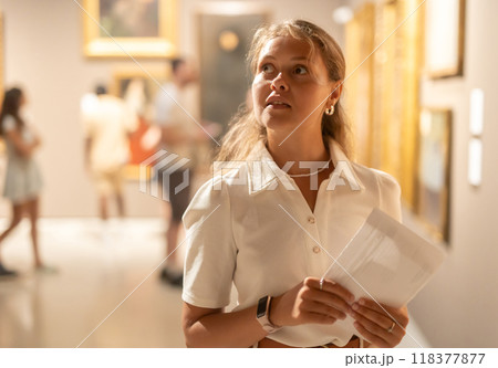 Woman with sheet piece of paper in hands view pictures and icons in museum hall 118377877