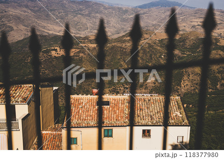 View through iron fence of rustic village house and mountainous landscape 118377980