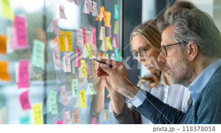A man and a woman are working on a whiteboard with colorful sticky notes 118378058