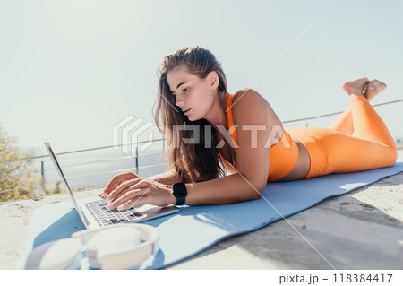 Woman in Orange Sportswear Working on a Laptop Outdoors Woman in Orange Sportswear Working on a Laptop Outdoors 118384417