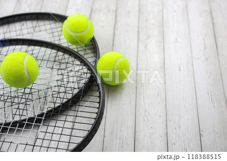 Two tennis rackets lie on top of each other on the left of the photo, yellow tennis balls against a white tree background lie on them and next to them. High quality photo 118388515