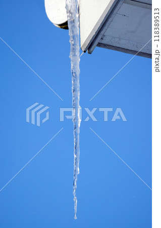 Transparent icicle hangs on a white gutter of rural house 118389513