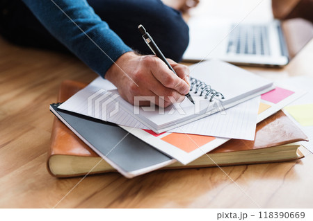 Close up of man writing notes in planner, working at desk from home. Telecommuting and home office. 118390669
