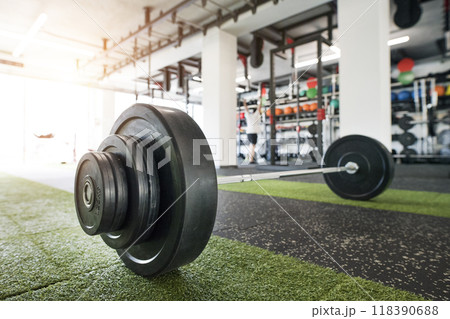 Barbell on gym floor. Rows of gym equipment, metal barbells, dubbells on racks for strength training in gym. 118390688