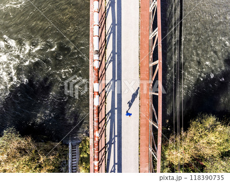 Aerial view of a runner running across bridge over the river. Morning running training. Aerial view of a runner running across bridge over the river. Morning running training. 118390735