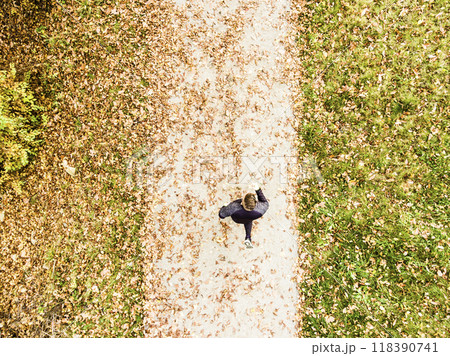 Aerial view of a runner running through autumn park on jogging path with fallen leaves. Morning running training. Aerial view of a runner running through autumn park on jogging path with fallen leaves. Morning running training. 118390741