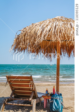 Straw beach umbrella and wooden sunbed on a sandy shore with the sea and blue sky 118393129
