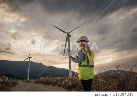 A Wind Energy Technician is meticulously inspecting a towering turbine set against a breathtaking scenic landscape, ensuring it operates efficiently and contributes to sustainable energy production 118394339