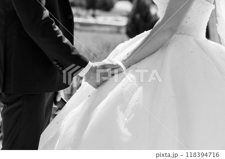 Romantic Black and White Close-Up of Bride and Groom Holding Hands on Wedding Day, Showcasing Elegant Gown and Suit 118394716