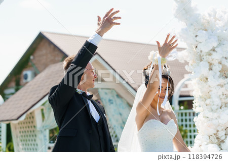 Elegant Outdoor Wedding Ceremony with Joyful Couple Under Floral Arch 118394726