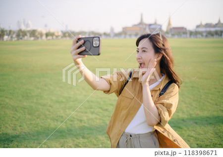 Traveler asian woman in her 30s making a livestream or selfie on smartphone while explores the grandeur of Wat Pra Kaew. Discover the religious significance and historical heritage with her. Traveler asian woman in her 30s making a livestream or selfie on smartphone while explores the grandeur of Wat Pra Kaew. Discover the religious significance and historical heritage with her. 118398671
