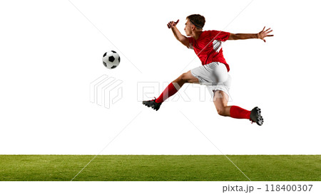Young footballer in red and white, leaping high to control ball, performing skillful header during football training on green field in studio. 118400307