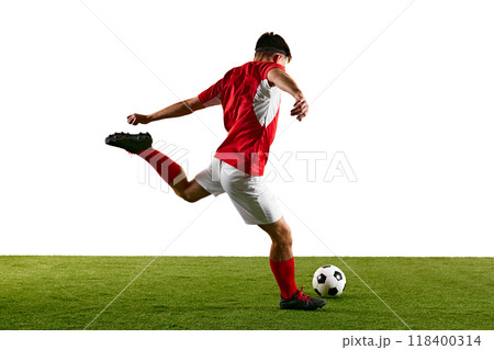 Determined football player in red-white, launching into jump-kick while training against white studio backdrop. Dynamic photo. Determined football player in red-white, launching into jump-kick while training against white studio backdrop. Dynamic photo. 118400314