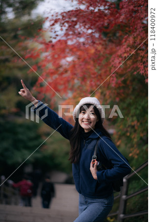 Asian woman in Japan's fall beauty, a cheerful holiday portrait in Kyoto. Vibrant foliage, friends, and smiles by the lake create a joyful and scenic atmosphere. 118400972