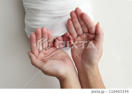 The palms of the parents. A father and mother hold the feet of a newborn child in a white blanket on a white background.. The feet of a newborn in the hands of parents. Photo of foot, heels and toes The palms of the parents. A father and mother hold the feet of a newborn child in a white blanket on a white background.. The feet of a newborn in the hands of parents. Photo of foot, heels and toes 118403334