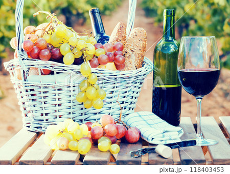 Still life with glass of red wine grapes and picnic basket on table 118403453