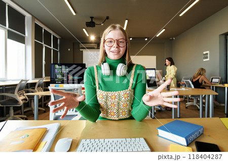 POV of young woman wearing glasses smiling at camera and gesturing while speaking via video chat in school classroom 118404287