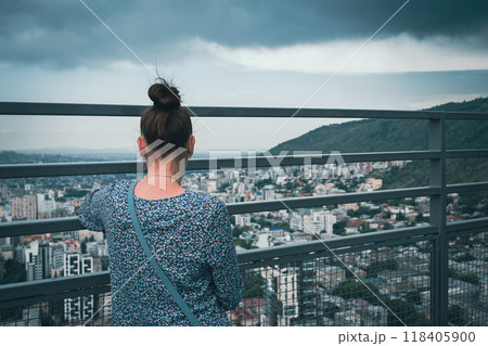 Woman overlooking a cityscape from a high viewpoint against a cloudy sky Woman overlooking a cityscape from a high viewpoint against a cloudy sky 118405900