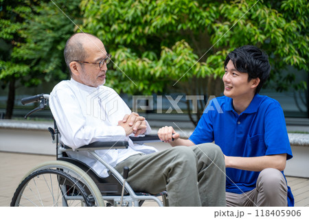 車いすのシニア男性と介護施設スタッフの手元 118405906