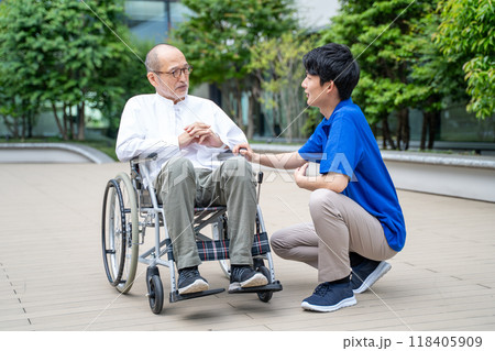 車いすのシニア男性と介護施設スタッフの手元 118405909