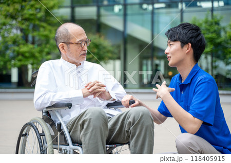 車いすのシニア男性と介護施設スタッフの手元 車いすのシニア男性と介護施設スタッフの手元 118405915