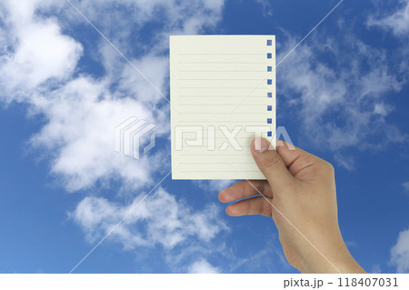 Hand holding a empty note paper with a background of blue sky and white clouds. Hand holding a empty note paper with a background of blue sky and white clouds. 118407031