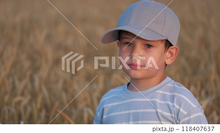 Portrait of boy child kid in nature in wheat field. Thoughtful tired sweaty after long game kid child boy breathing heavily, standing in agricultural yellow field meadow lawn among ears of wheat. Portrait of boy child kid in nature in wheat field. Thoughtful tired sweaty after long game kid child boy breathing heavily, standing in agricultural yellow field meadow lawn among ears of wheat. 118407637