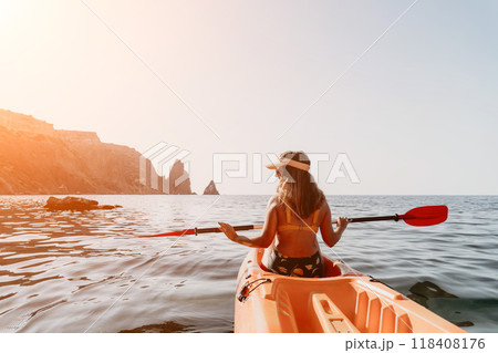 Kayaking Woman Sea Coastline - Woman paddling orange kayak in the sea with mountains in the background. 118408176