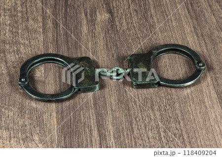 Metal handcuffs lie on a wooden table. On the wooden table lie the metal handcuffs 118409204