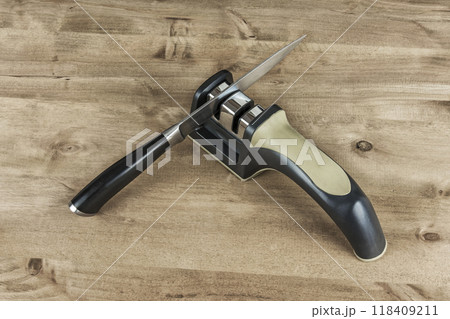 A metal knife with a plastic handle and a sharpener on a wooden surface 118409211