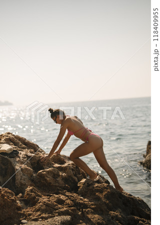 A woman is energetically climbing rocks at the seaside under the warm summer sunlight 118409955