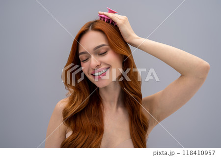 Ginger young woman massaging her head with a scalp massager Ginger young woman massaging her head with a scalp massager 118410957
