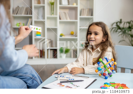 Cute girl having an educational session with a speech therapist and looking involved 118410973