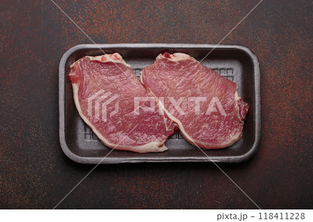 Raw pork steaks lying in black plastic tray on dark background top view 118411228