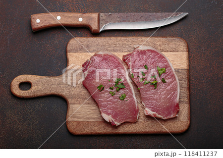 Raw pork steaks with spices on wooden chopping board top view 118411237