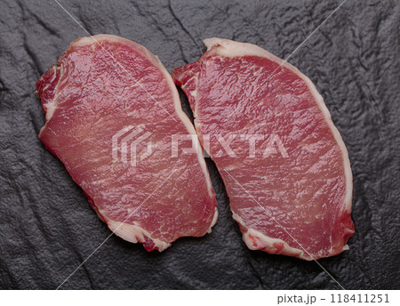 Raw pork loin steaks resting on black slate plate top view Raw pork loin steaks resting on black slate plate top view 118411251