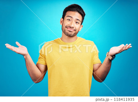 Confused, question and portrait of man shoulder shrugging and raise arms isolated in a blue studio background. Clueless, smile and young male person with doubt, whatever and doing a hand gesture 118411935