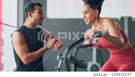 Fitness, training on an exercise bike and a woman with her coach in the gym to time her speed on a sports watch. Exercise, motivation and a personal trainer with a young athlete for workout support 118412037