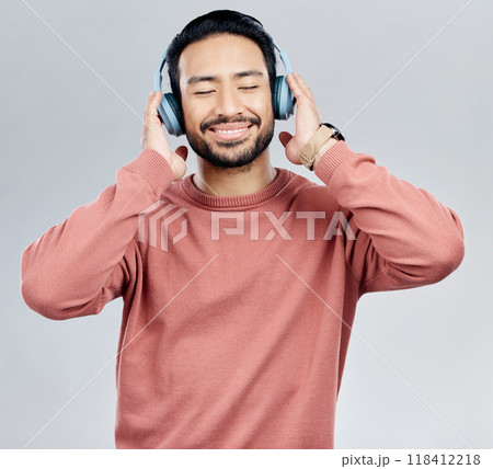 Listen, happy and Asian man with headphones, streaming music and sounds against a white studio background. Japan, male and guy with headset, listening to radio and podcast for motivation and wellness 118412218