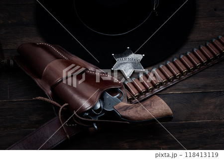 Old west sheriff star badge with gun, holster and gun belt with old west hat on table. Top view. 118413119
