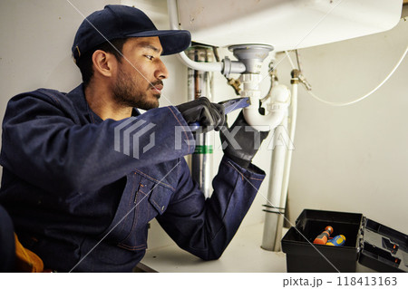 Plumbing, pipes and maintenance with man in kitchen for repair, industrial and inspection. Handyman, tools and safety with male plumber fixing sink for home improvement, drainage and water system Plumbing, pipes and maintenance with man in kitchen for repair, industrial and inspection. Handyman, tools and safety with male plumber fixing sink for home improvement, drainage and water system 118413163