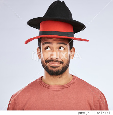 Confused, hats and young man in a studio with a thinking, idea or contemplating face expression. Pensive, thoughtful and Indian male person with fun head accessories isolated by a white background. Confused, hats and young man in a studio with a thinking, idea or contemplating face expression. Pensive, thoughtful and Indian male person with fun head accessories isolated by a white background. 118413471