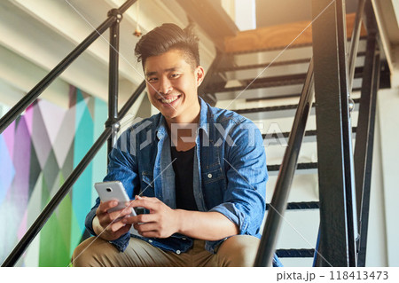 Asian man, office stairs and texting with phone in portrait with chat, smile and social network app. Young japanese creative, web design startup and relax on steps in workplace, contact and cellphone 118413473